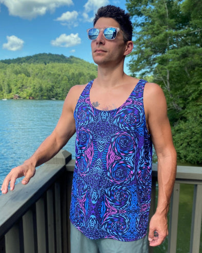 Mid shot photograph of a male model from the waist up in the foreground wearing a Bleace psychedelic tank top with pink, turquoise and purple swirls on it with Lake Rabun, Georgia in the background.